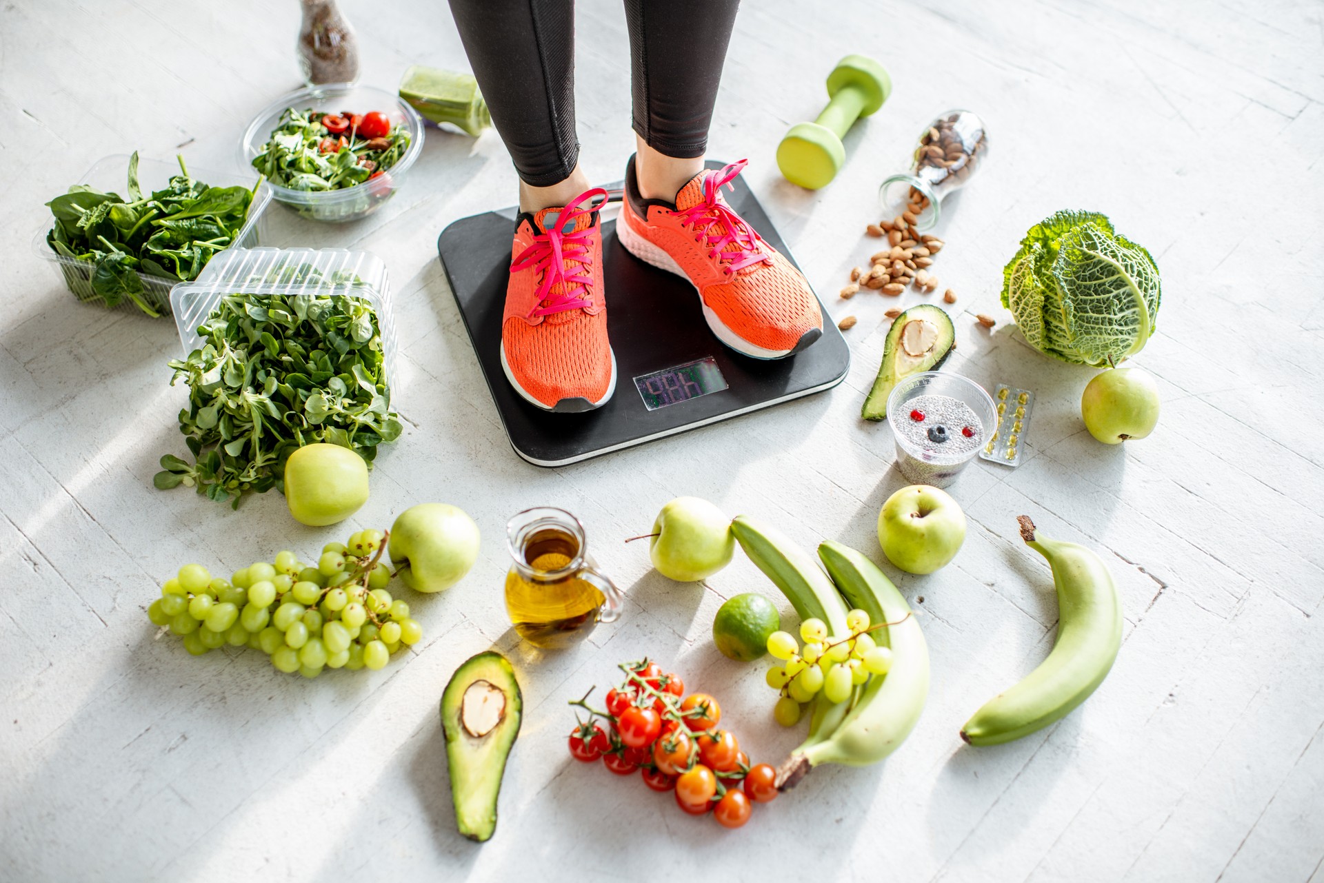 Sports woman weighing with healthy food around